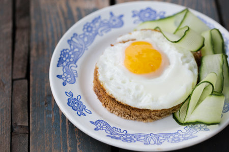 A fried egg on a round piece of bread with a cucumberの写真素材