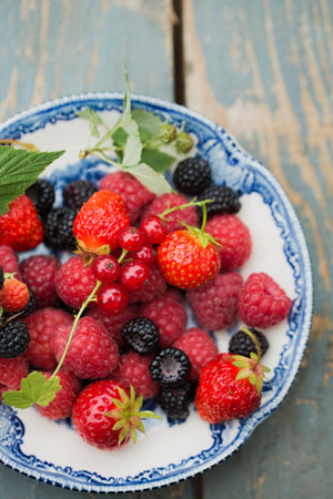 Ripe raspberries, strawberry and wild blackberries on a vintage plateの写真素材