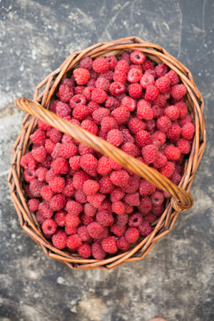 A wicker basket full of ripe raspberries on the tableの写真素材