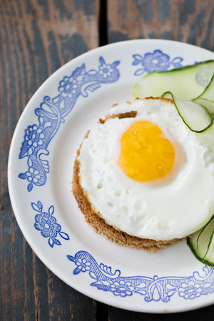 A fried egg on a round piece of bread with a cucumberの写真素材