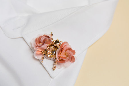 Handmade brooch made of stones and sequins on the collar of a white shirt on a beige backgroundの写真素材