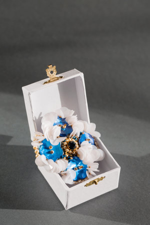 Handmade brooch with mother-of-pearl blue buttons and white sequins in a small box on a gray backgroundの写真素材