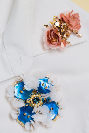 Two decorative handmade brooches on the collar of a white shirtの写真素材