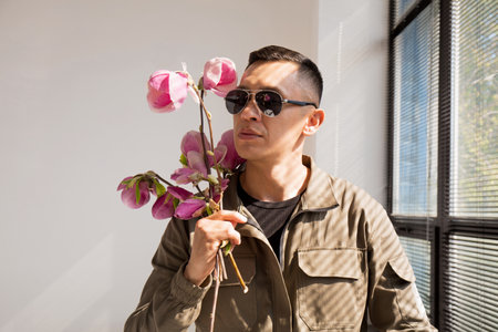A man in sunglasses with a bouquet of magnolia near a window with sunlightの写真素材
