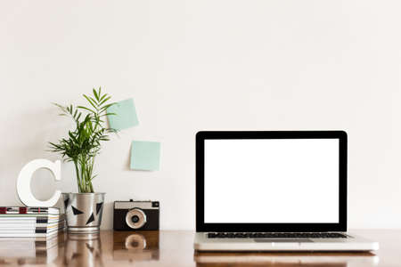 Cropped shot of modern workspace with blank screen laptop, stationery and copy space on white wall backgroundの写真素材