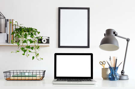 Laptop computer mockup at home office desk with poster frame, camera, design lamp. books and ivy on the shelf.の写真素材