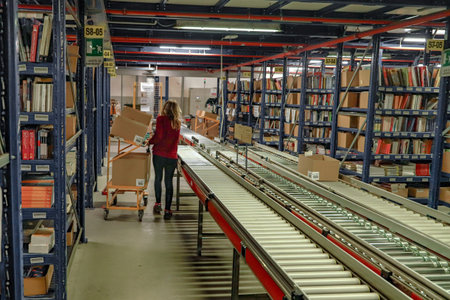 Warehouse interior. Woman in a red jacket is standing near the conveyor belt.の写真素材