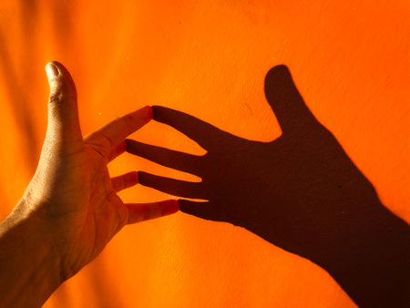 hand pointing at orange wall with shadow, closeup of photo. Man's hand and woman's hand on orange background. The shadow of the hands.の写真素材