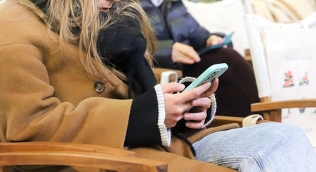 Woman using mobile phone sitting on a chair in a street cafe.