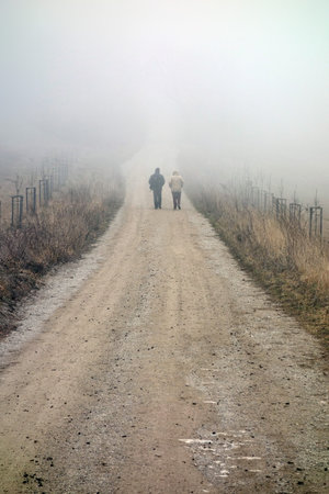 two unrecognizable Persons hiking along a foggy path