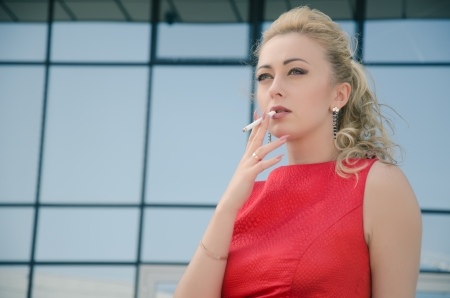 girl in red dress smoking on the street in summerの写真素材