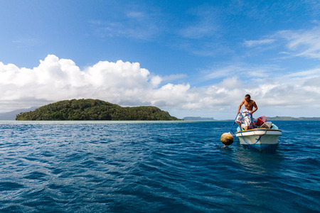 Pohnpei, Micronesia - Dec 27,2011: a local Micronesian in a boat man pulls a buoy out of the water with Pohnpei island in the background, Caroline islands, Federated States of Micronesia (FSM)のeditorial素材