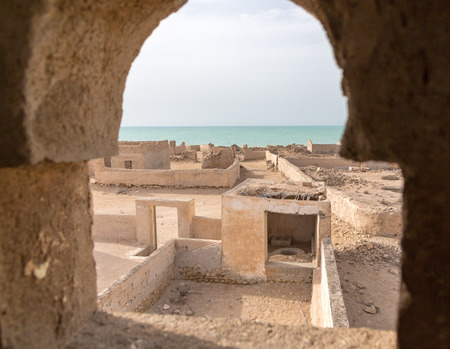 Ruined ancient old Arab pearling and fishing town Al Jumail, Qatar. The desert at coast of Persian Gulf. Abandoned mosque with minaret. Deserted village. A view out of minaret's window to the seaの写真素材