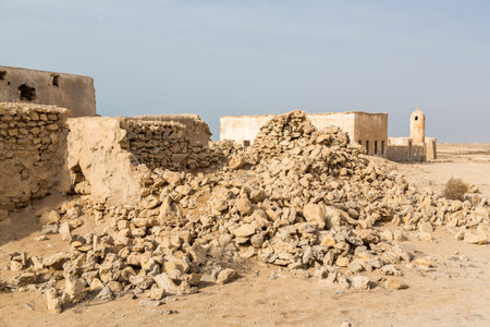 Ruined ancient old Arab pearling and fishing town Al Jumail, Qatar. The desert at coast of Persian Gulf. Abandoned mosque with minaret. Deserted village. Pile of stonesの写真素材