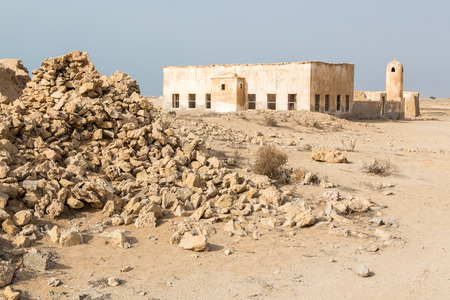 Ruined ancient old Arab pearling and fishing town Al Jumail, Qatar. The desert at coast of Persian Gulf. Abandoned mosque with minaret. Deserted village. Pile of stonesの写真素材