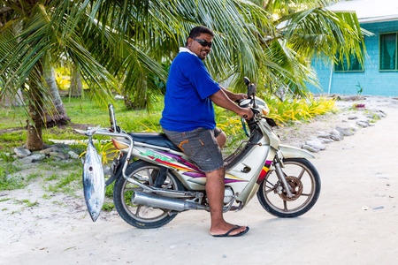 Vaiaku village, Tuvalu - Dec 27, 2014: A local native Polynesian man on a motorcycle (motorbike) with a tuna fish catch. Fongafale motu, Funafuti atoll, Polynesia, South Pacific Ocean, Oceania.のeditorial素材