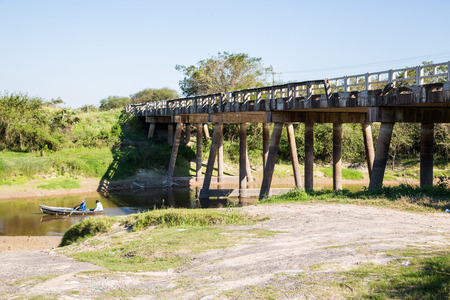 National Route 9 highway runs over a river bridge in Paraguayan Gran Chaco savannah, Paraguay. Ruta Nacional Numero 9 Dr. Carlos Antonio Lopez. Ruta Transchaco. Two men in a rowing boat.の写真素材
