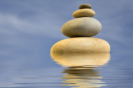 pile of zen round stones with blue sky and water reflexionの写真素材