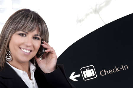 businesswoman with mobile phone in international airport - check-in billboard in backgroundの写真素材