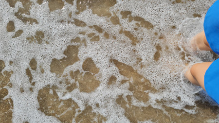 Woman's feet on the beach with sea foam. Top view.の写真素材