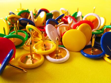 Multicolored buttons, cloves on a yellow background. Stationery nails for fastening paper.の写真素材
