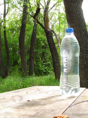 A transparent water bottle on a wooden old table in the fresh air near the river in the valley where many plants, trees and green nature nature.の写真素材