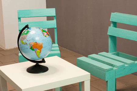 A coffee table and a wooden chair near a gray wall. Globe, travel agency office.