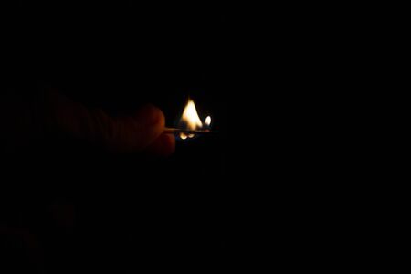 burning match in hand on a black background.の写真素材