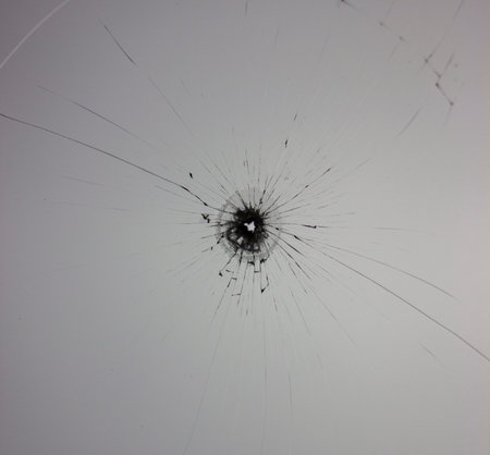 A bullet hole in a window damaged by bullies showcase. Broken glass on the window