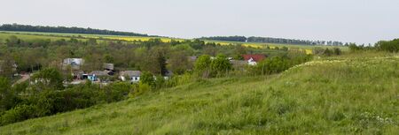 A small village in the valley, thick trees and houses lined up between the fields.の写真素材