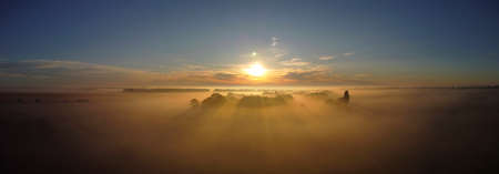 Morning fog and sunlight illuminating the cream of the trees. Panoramic shot of rural nature, view from the drone.の写真素材