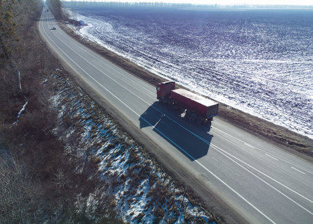 Truck on the asphalt road outside the city. Winter sunny day. Aerial view of the road