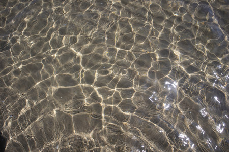 Clear sea water with sunlight creating shimmering patterns on the sandy bottom