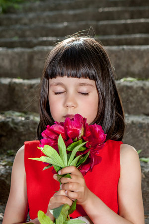 Charming little girl in a red dress sitting on stairs with peony closed eyesの写真素材