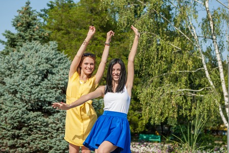 Beauties in style. Two beautiful young well-dressed women smiling at camera while standing with arms raised funny outdoorsの写真素材