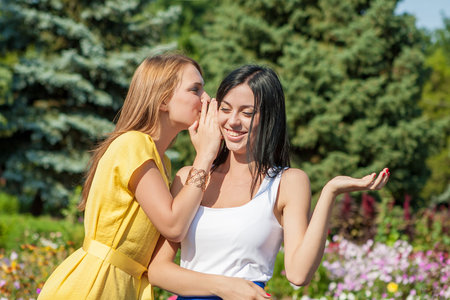 Friendly talk. Two beautiful young women walking near the flowerbed and talkingの写真素材