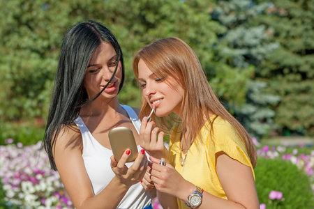 young Girls Applying Make up and Looking in the Mirror. Pretty Teens Having Fun and Putting Makeup Lipstick or Lip gloss. women Outdoors. Cosmeticsの写真素材