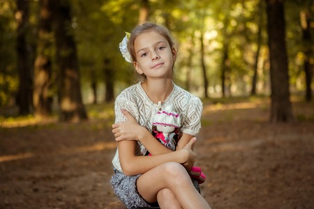 Charming little girl standing near  tree in forest with  doll in handsの写真素材