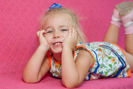 Adorable little girl lying on pink  background. Capricious, sad.の写真素材