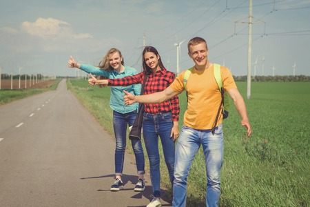 Young hipster friends on road. Two girls and a guy travel hitchhikers. Retro tonedの写真素材