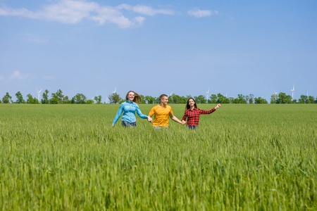 Young happy Friends running on green wheat field. One guy and two girls are jumping, having fun.の写真素材