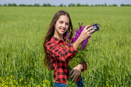 Young girl making selfie. Beautiful young women making selfie and grimacing. In  field with flowersの写真素材