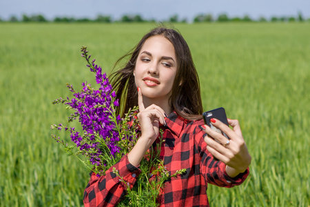 Young girl making selfie. Beautiful young women making selfie and grimacing. In  field with flowersの写真素材