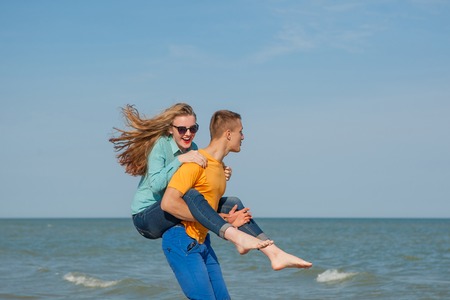 Happy young joyful guy and girl having fun on the beach, laughing together. During summer holidays vacation on sea. Beautiful energetic couple friends adolescents.の写真素材