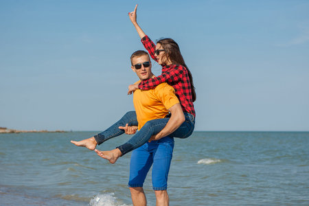 Happy young joyful guy and girl having fun on the beach, laughing together. During summer holidays vacation on sea. Beautiful energetic couple friends adolescents.の写真素材