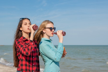 Friends and juice or smoothie. Two young cheerful girls with juice and buns smiling  on background of blue skyの写真素材