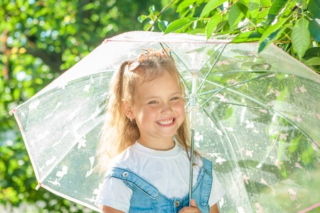 Happy child in the summer sunny rain. Funny little girl playing outdoors hot day with umbrella. Joyful emotionsの写真素材
