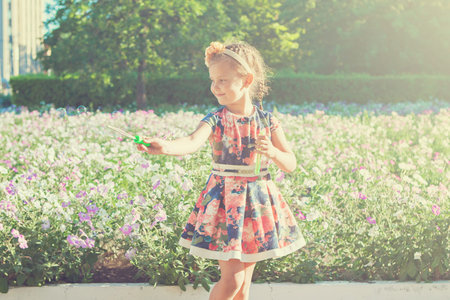 Happy little girl with soap bubbles. Near flower bedの写真素材