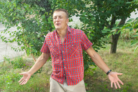 Sexy young man in rain. Pleasure cool rain in summer on background of treesの写真素材