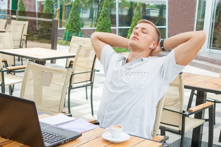 Young man in headphones working on laptop while sitting at sidewalk cafeの写真素材